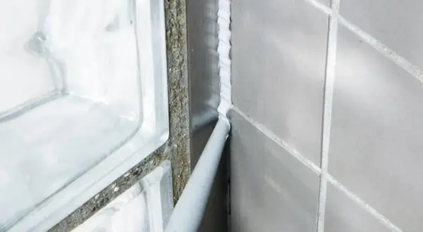 Foga om badrummet med silikon. En fogpistol applicerar ny vit silikon längs en vägg med grå kakelplattor och en duschvägg av glasblock.