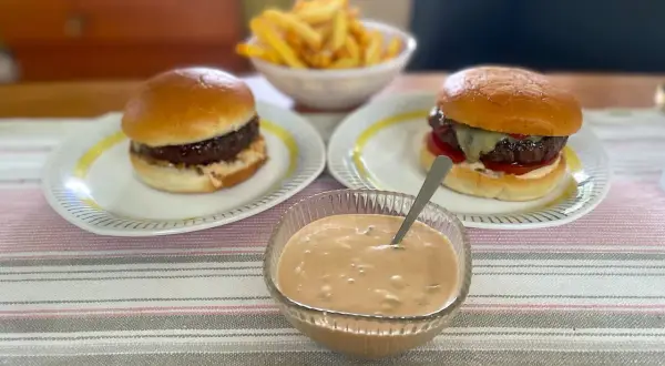 Två saftiga hamburgare med pommes frites och en skål med krämig hamburgerdressing. Perfekt för en mysig hemmakväll!