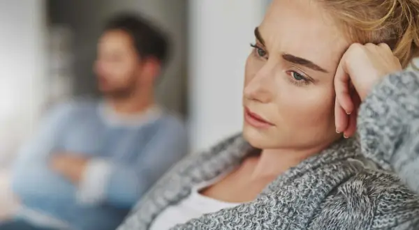 En kvinna med en bekymrad blick vilar huvudet mot handen. I bakgrunden sitter en man med armarna i kors, kanske en symbol för att han är emotionellt omogen.