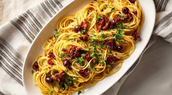En skål med spaghetti toppad med soltorkade tomater, oliver och persilja. Ett enkelt och gott pasta recept.