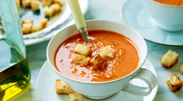 En skål med krämig gazpacho, toppad med krutonger. Bredvid står en karaff med olivolja, perfekt för ditt gazpacho recept.