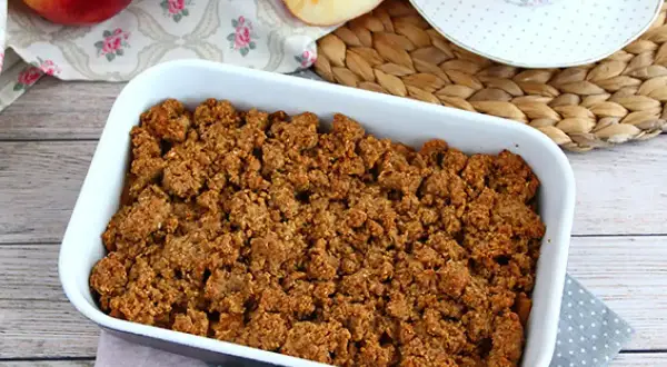 En härlig glutenfri frukost med äppelcrisp i en vit form, äpplen och en kopp te i bakgrunden.