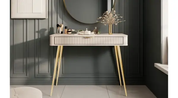 Ett elegant sminkbord med guldfärgade ben och en räfflad lådfront. Inspiration för ett stilfullt sminkbord med smink, parfym och en vas med blommor.