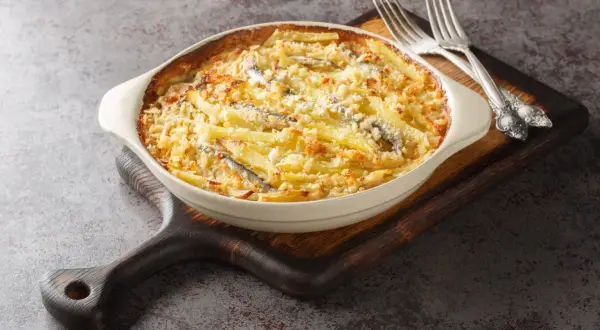 En krämig Janssons frestelse med potatis, ansjovis och ströbröd i en ugnsform, redo att serveras med gafflar.