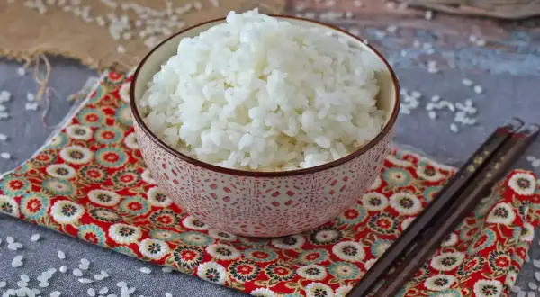 Perfekt sushiris i en vacker skål, redo för ditt sushirecept. Ätpinnar ligger bredvid.