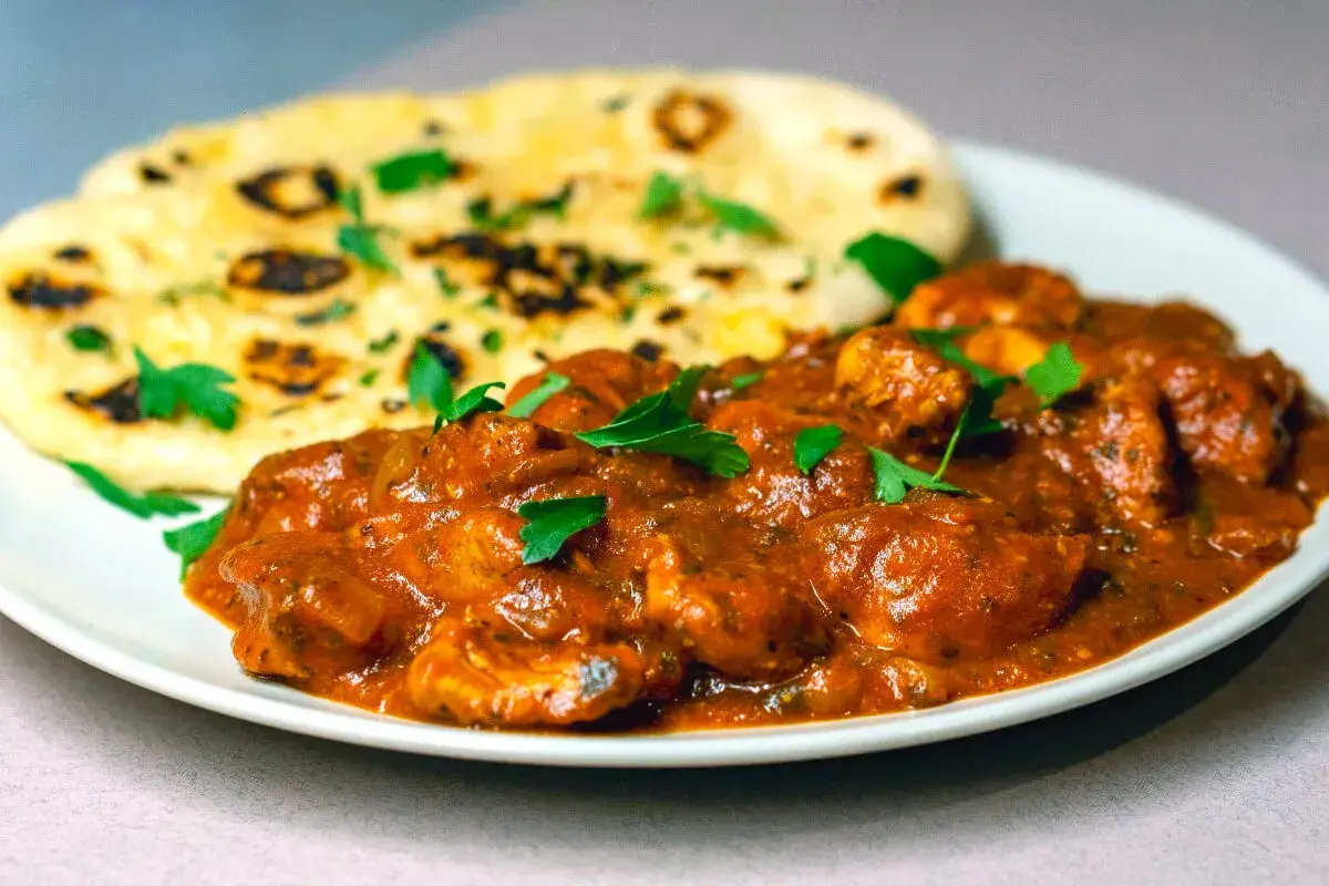 En krämig chicken tikka masala med naanbröd, garnerad med färsk persilja.