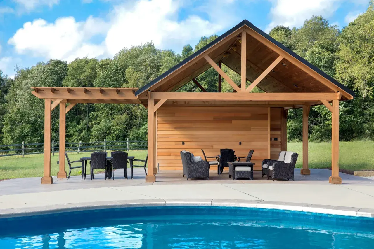 En stor träpergola med tak och sittgrupper vid en blå pool. Kanske är det här man behöver pergola bygglov för att skapa en perfekt uteplats.
