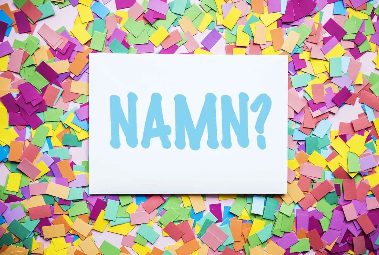 En vit skylt med texten "NAMN?" i ljusblått, omgiven av färgglatt konfetti. Kanske ett unisex namn ska väljas?