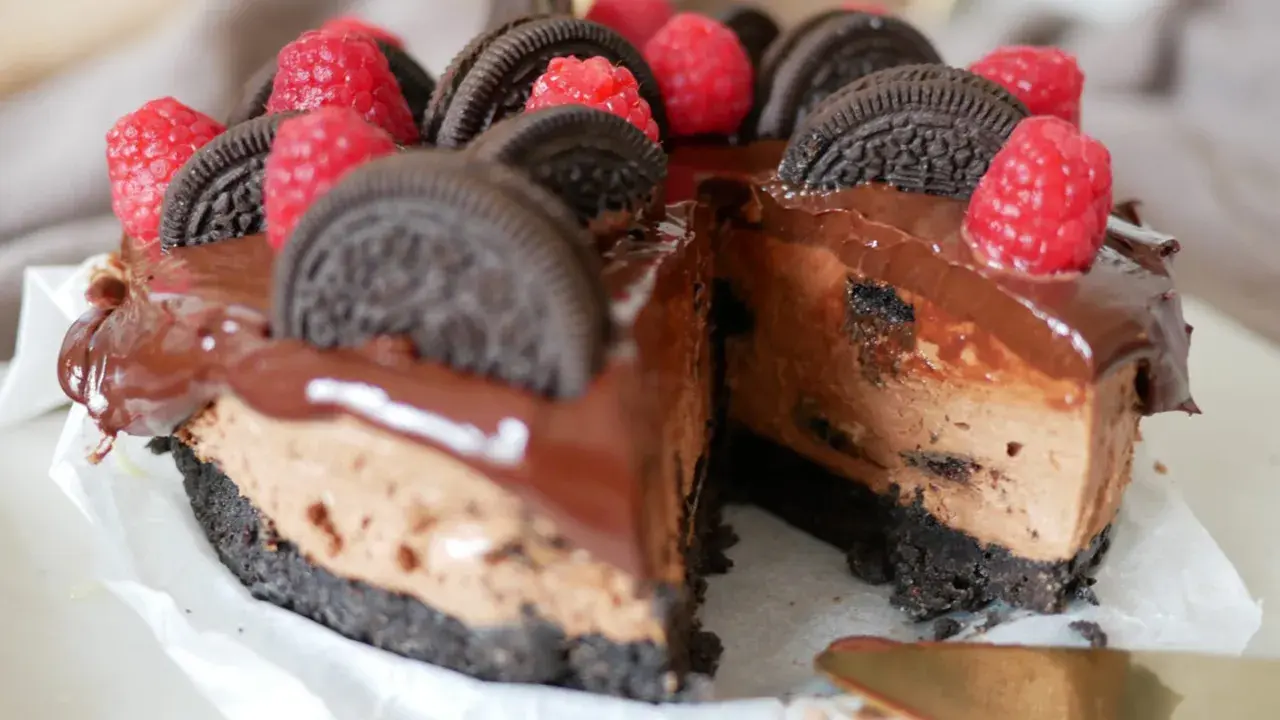 En chokladig oreo cheesecake med hallon och chokladglasyr. En bit är bortskuren.