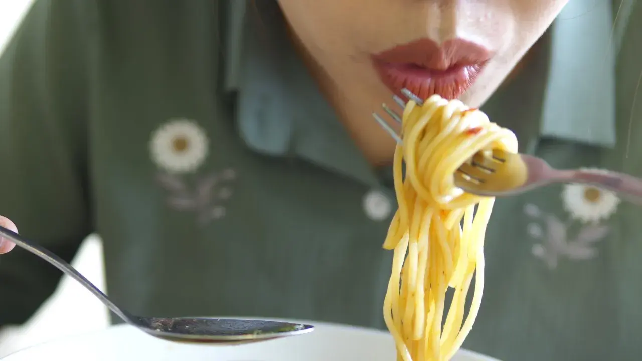 En person äter spaghetti med gaffel och sked. Det är en härlig pastarätt.
