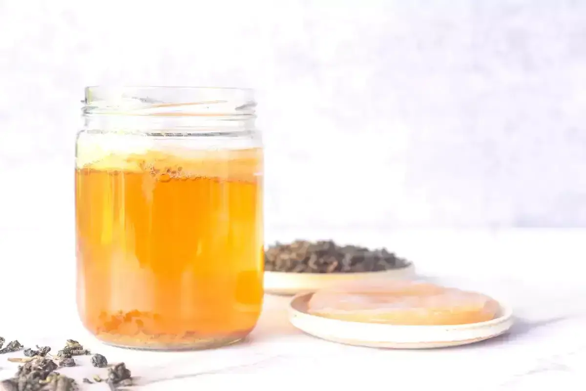 En burk med fermenterad dryck, teblad och en SCOBY. Perfekt för ditt kombucha recept.