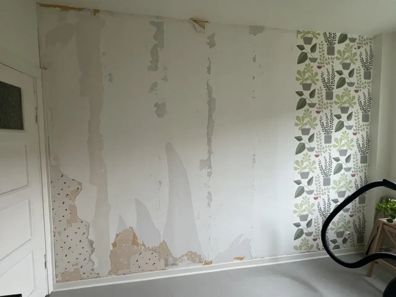 Väggen är delvis avrivet tapet, med fläckar av gammal tapet kvar. En bit med blommig tapet syns till höger.