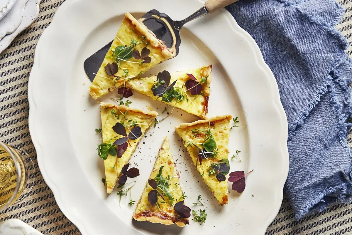 Välskuren quiche lorraine med gyllene skorpa, toppad med färska örter och mörklila blad. Perfekt för en lätt lunch.