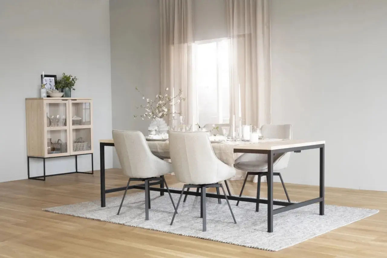 Ett ljust och luftigt rum med matbord och stolar i skandinavisk design. Ett vitrinskåp i trä och glas står till vänster.