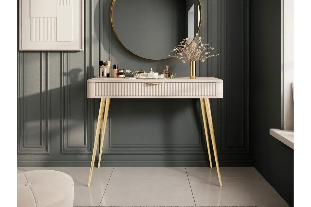 Ett elegant sminkbord med guldfärgade ben och en räfflad lådfront. Inspiration för ett stilfullt sminkbord med smink, parfym och en vas med blommor.