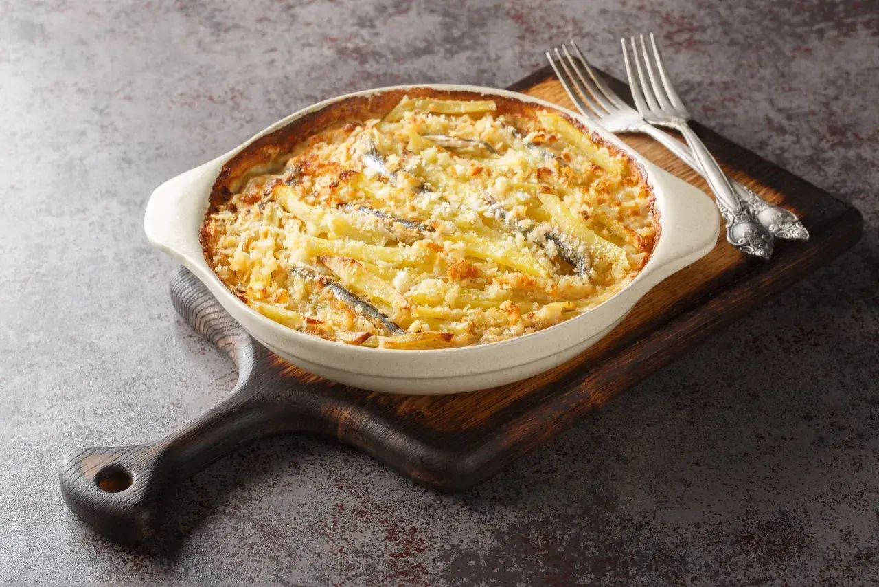En krämig Janssons frestelse med potatis, ansjovis och ströbröd i en ugnsform, redo att serveras med gafflar.