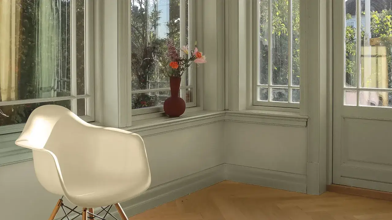 En ljus hall med en vit stol och en vas med blommor p&aring; f&ouml;nsterbr&auml;dan. V&auml;ggarna &auml;r m&aring;lade i en ljusgr&ouml;n nyans.