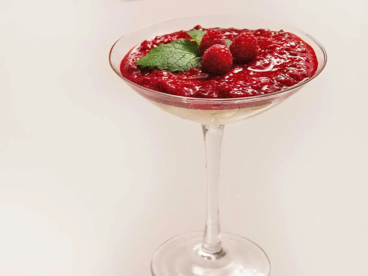 En l&auml;cker fryst cheesecake i ett glas, toppad med hallons&aring;s, f&auml;rska hallon och mynta.