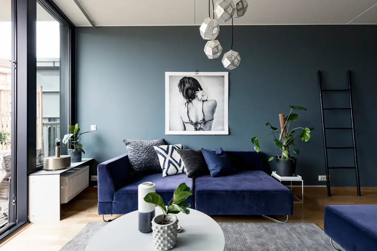 En lyxig bl&aring; soffa med sammetsyta ger inspiration till ett modernt vardagsrum. Konstverk och v&auml;xter kompletterar den stilfulla inredningen.