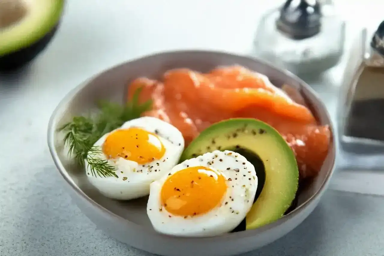 En sk&aring;l med en perfekt keto diet frukost: kokta &auml;gg, lax och avokado.