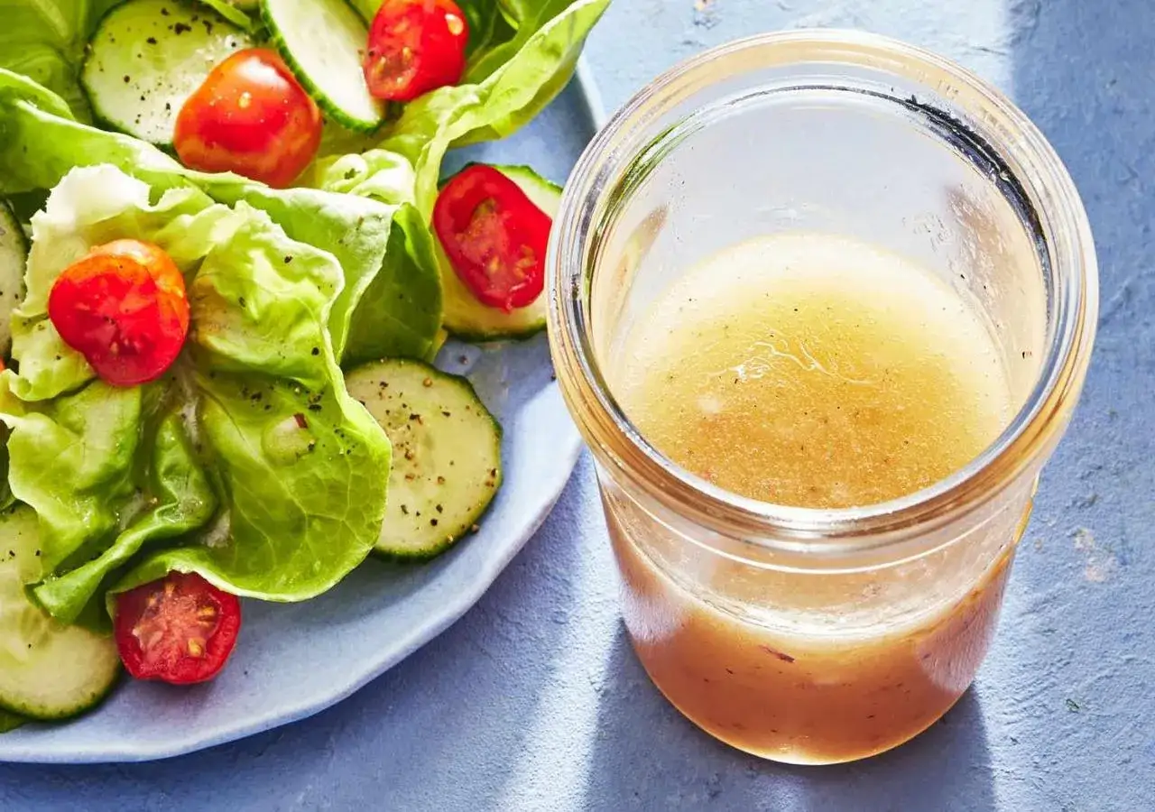 En burk med gyllene dressing till sallad står bredvid en fräsch sallad med gurka och tomater.