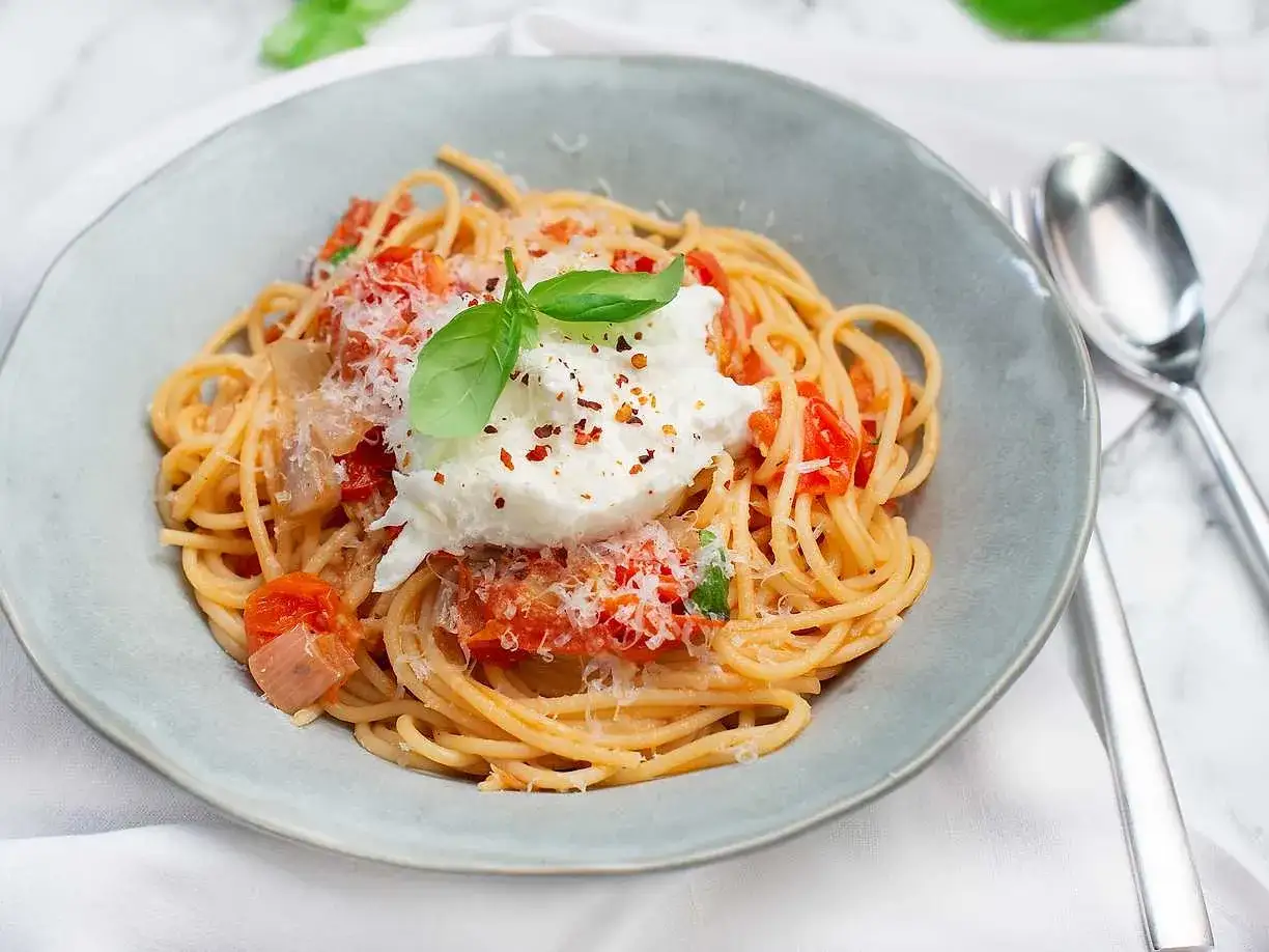 En kr&auml;mig burrata p&aring; en tallrik spaghetti med tomats&aring;s och basilika. Ett perfekt pasta recept f&ouml;r en snabb och god middag.
