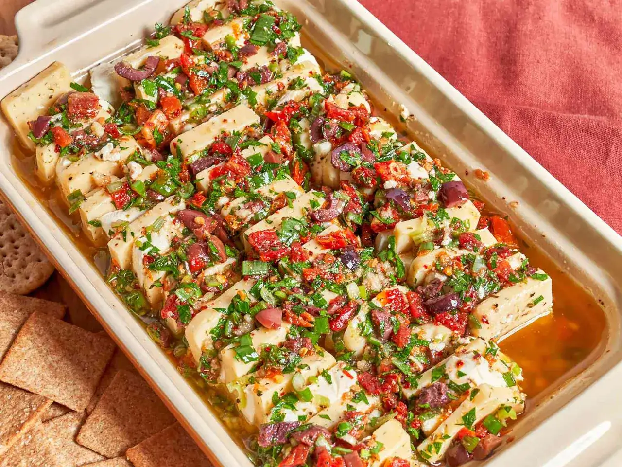 Ugnsbakad fetaost med soltorkade tomater, oliver och &ouml;rter, ett perfekt medelhavskost recept. Serveras med kex.