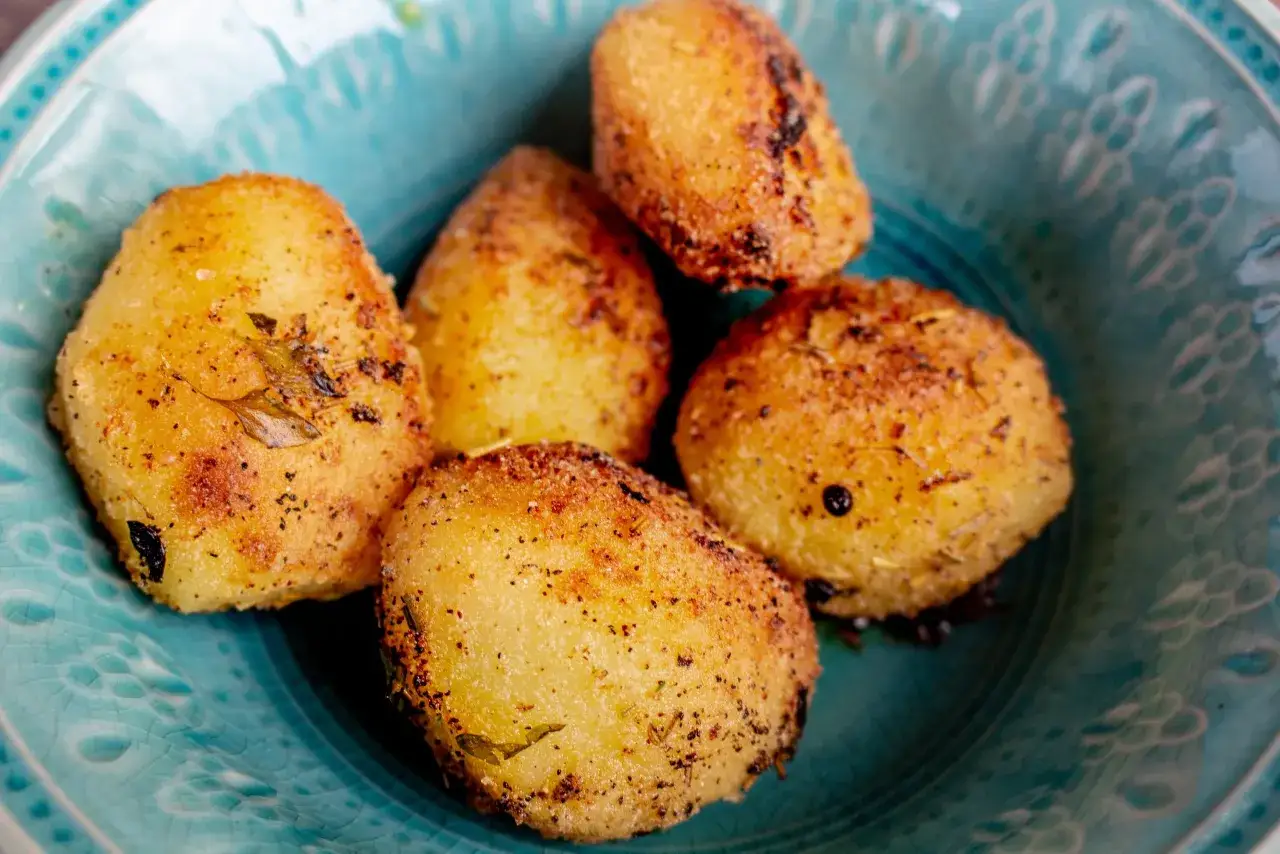 Fem gyllene, r&aring;stekt potatis med &ouml;rter och peppar i en vacker turkos sk&aring;l. Perfekt som tillbeh&ouml;r!