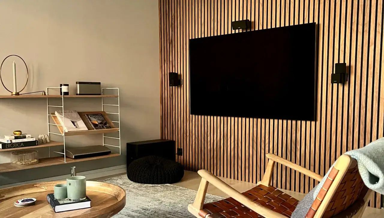 Snyggt vardagsrum med en stor TV inbyggd i en v&auml;gg av tr&auml;ribbor. En bekv&auml;m f&aring;t&ouml;lj och ett runt soffbord kompletterar rummet.
