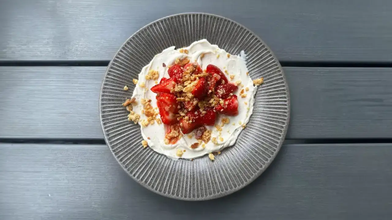 En tallrik med krämig dessert toppad med saftiga, limemarinerade jordgubbar och smulor. En härlig sommarfavorit!