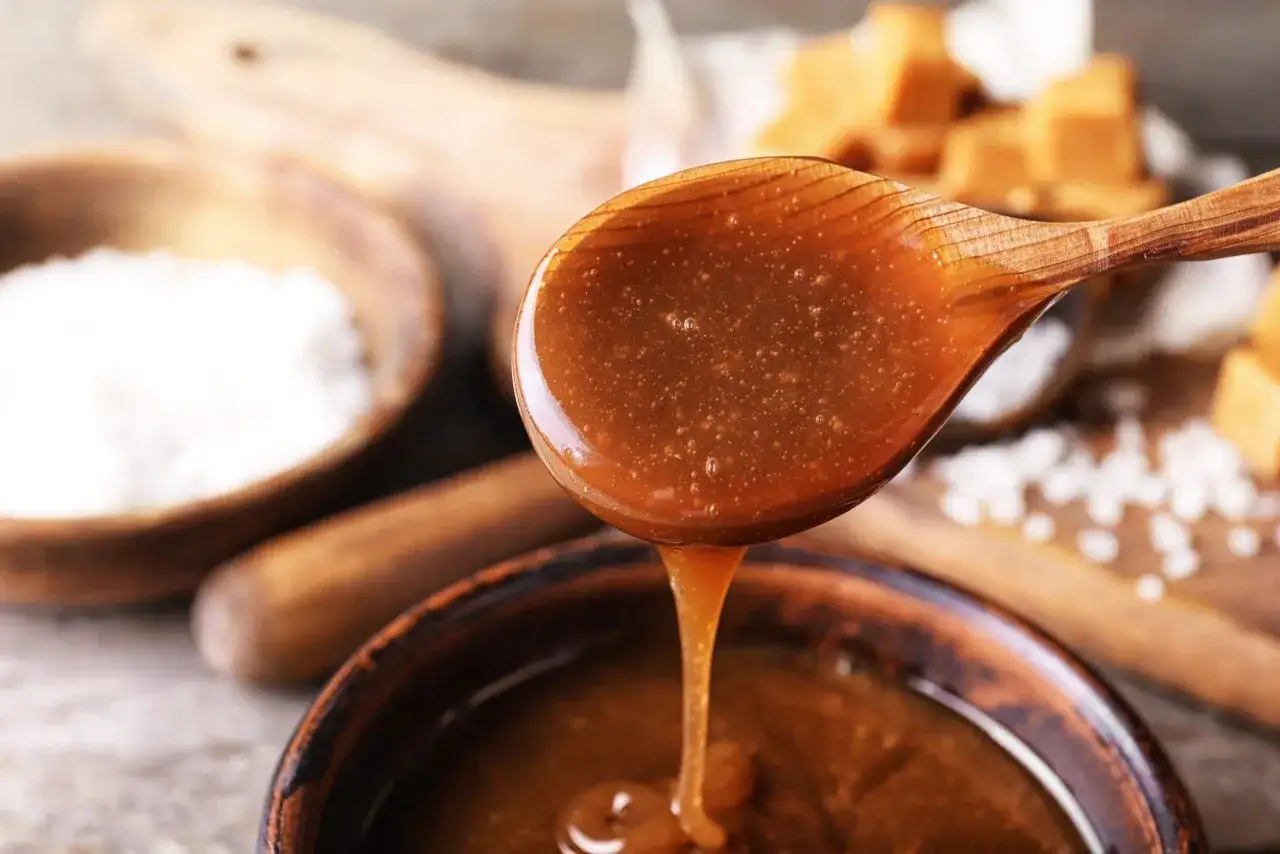 En sked med h&auml;rlig kolas&aring;s som droppar ner i en sk&aring;l. Ingredienser f&ouml;r ett enkelt kolas&aring;s recept syns i bakgrunden.