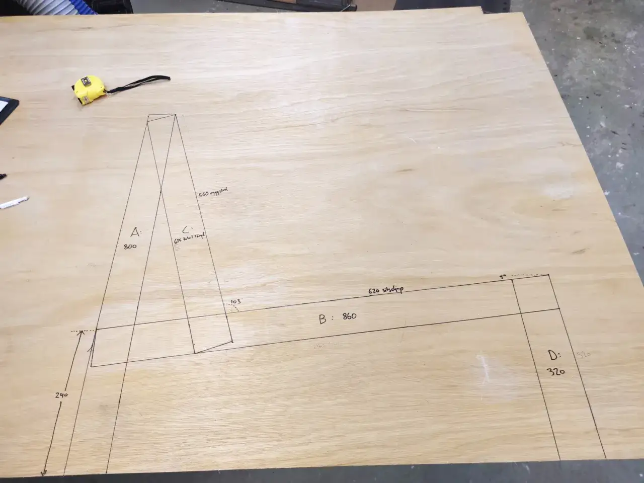 En ritning p&aring; en plywoodskiva visar m&aring;tt och linjer f&ouml;r att bygga en soffa. En gul m&auml;tband ligger bredvid.