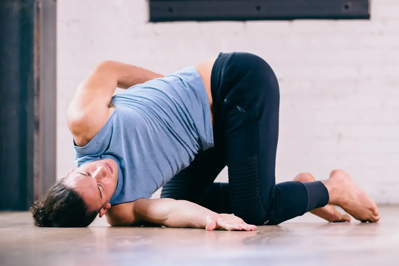Man i bl&aring; tr&ouml;ja och svarta byxor g&ouml;r en djup ryggb&ouml;j p&aring; golvet. Kan vara en del av yinyoga, men var uppm&auml;rksam p&aring; biverkningar.