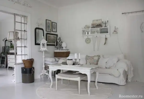 Ett rum med shabby chic inredning. En vit soffa med kuddar, ett vitt bord med ljus och en rund matta.