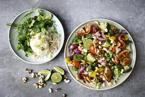 Två tallrikar med nyttig mat: en med ris, koriander och lime, den andra med kyckling, grönsaker och cashewnötter.