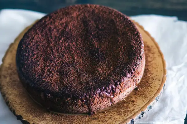 En gudomlig glutenfri chokladkaka, pudrad med kakao, serverad på en träskiva.