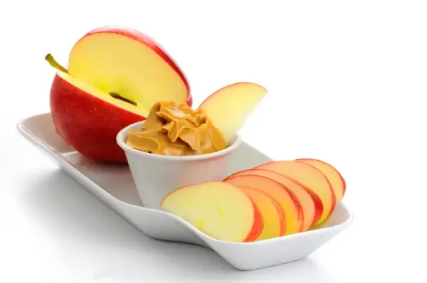 Ett rött äpple, skivat och med en skål jordnötssmör, perfekta kalorisnåla snacks.