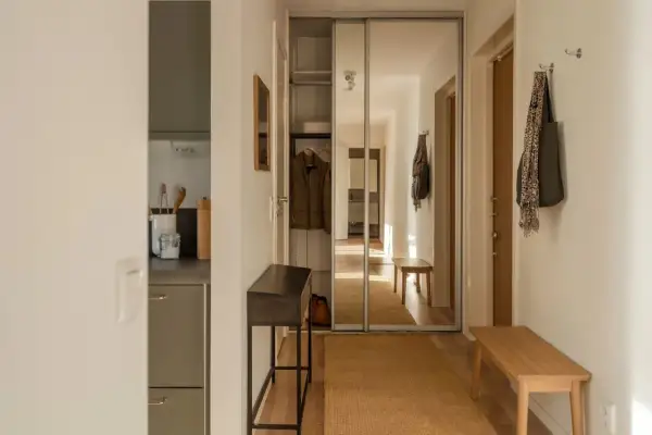 En ljus och inreda hall med en spegelgarderob, en smal konsol, en träbänk och en matta.