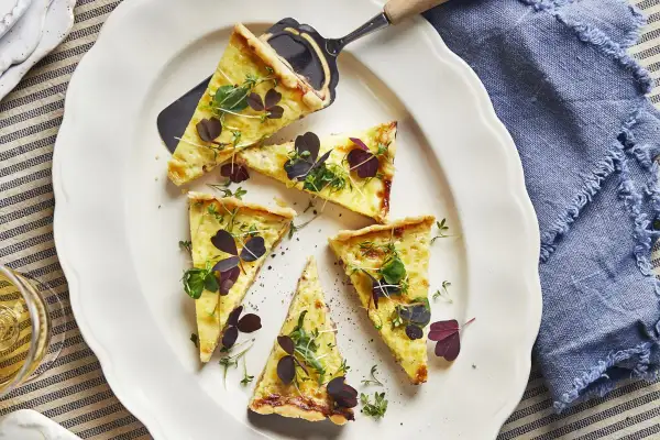 Välskuren quiche lorraine med gyllene skorpa, toppad med färska örter och mörklila blad. Perfekt för en lätt lunch.