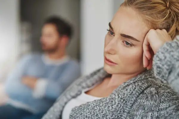 En kvinna med en bekymrad blick vilar huvudet mot handen. I bakgrunden sitter en man med armarna i kors, kanske en symbol för att han är emotionellt omogen.