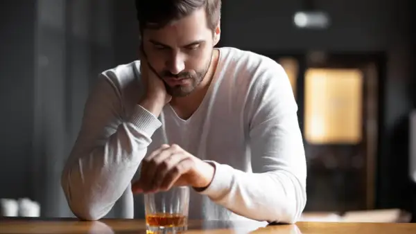 En man sitter ensam vid ett bord med ett glas whisky framför sig. Han ser nedstämd ut, som om min man dricker varje dag och han inte kan sluta.