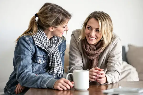 Två kvinnor ler mot varandra över en kaffemugg. De ser ut att vara vänner som pratar, inte alls som otacksamma vuxna barn.