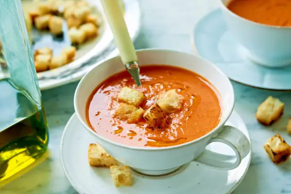En skål med krämig gazpacho, toppad med krutonger. Bredvid står en karaff med olivolja, perfekt för ditt gazpacho recept.