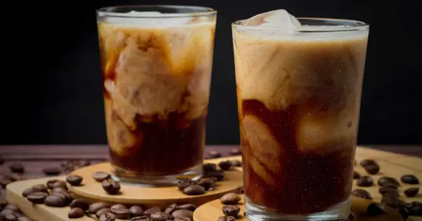 Två glas med krämigt iskaffe, perfekt för ett enkelt iskaffe recept. Kaffebönor sprider sig runt glasen.